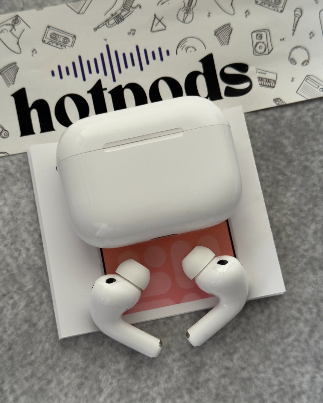 White wireless earbuds in a charging case on a gray surface with 'hotmods' branding in the background.